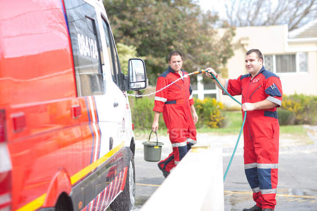 Paramédicos limpiando ambulancia con manguera - foto de stock