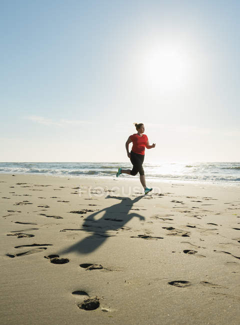Mujer madura corriendo en una playa al atardecer - foto de stock