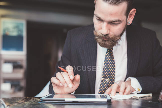Empresario haciendo notas del diario de la tableta digital en la mesa de café - foto de stock