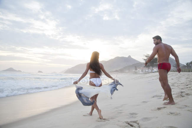 Mid adult couple on beach, walking towards ocean, rear view — Stock Photo