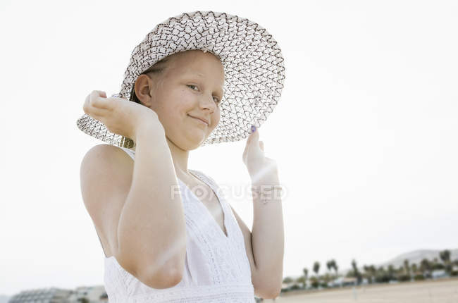Retrato de niña sosteniendo sombrero de sol en retroiluminación en la playa - foto de stock
