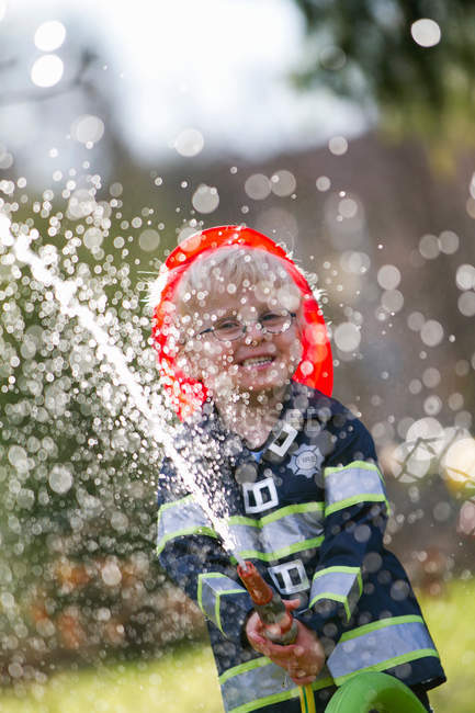 Boy in fireman costume playing with hose — Stock Photo