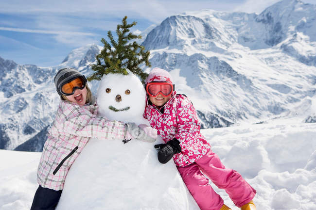 Две девушки со снеговиком — стоковое фото