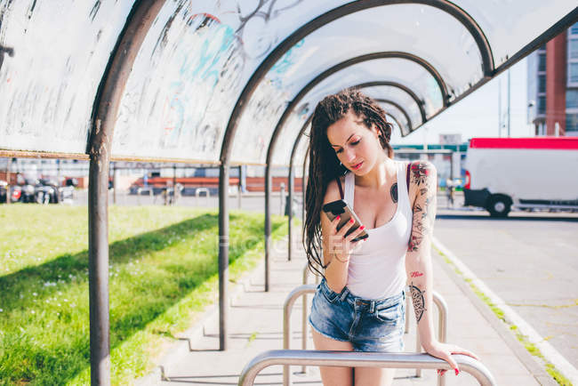Giovane donna con dreadlocks smartphone lettura in autobus urbano rifugio — Foto stock