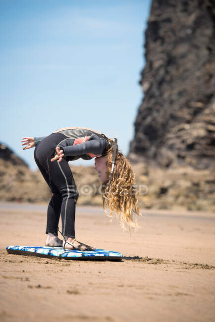 Девушка в гидрокостюме играет с доской для серфинга — стоковое фото