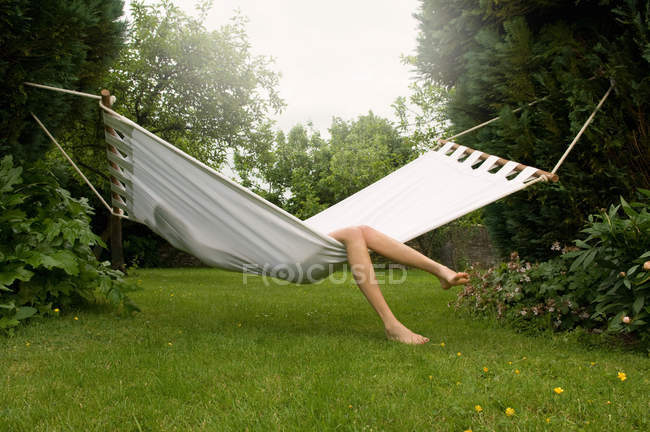 Pernas de mulher relaxante na rede em vegetação exuberante — Fotografia de Stock