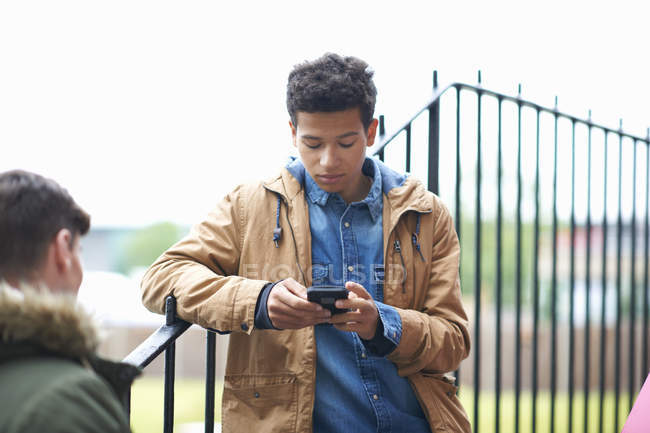 Молодой студент колледжа читает смс на смартфоне в кампусе — стоковое фото