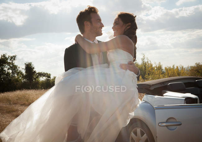 Noivo recém-casado transportando noiva ao ar livre — Fotografia de Stock