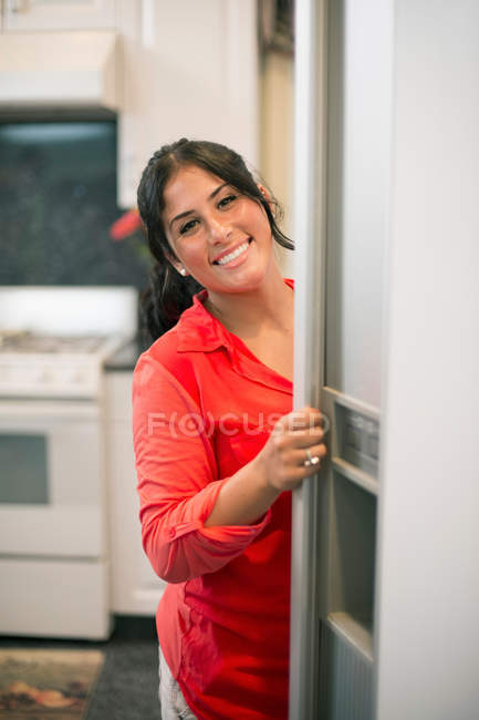 Усміхнена жінка відкриває двері холодильника — стокове фото