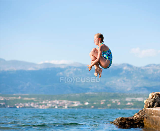 Девушка прыгает в воду с гор на заднем плане — стоковое фото