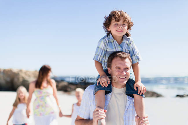 Father carrying son on shoulders, woman with daughters in background — Stock Photo