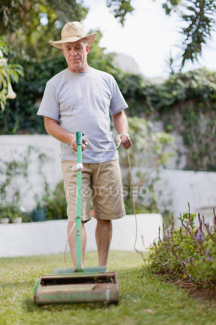 Homem mais velho cortando gramado no quintal — Fotografia de Stock