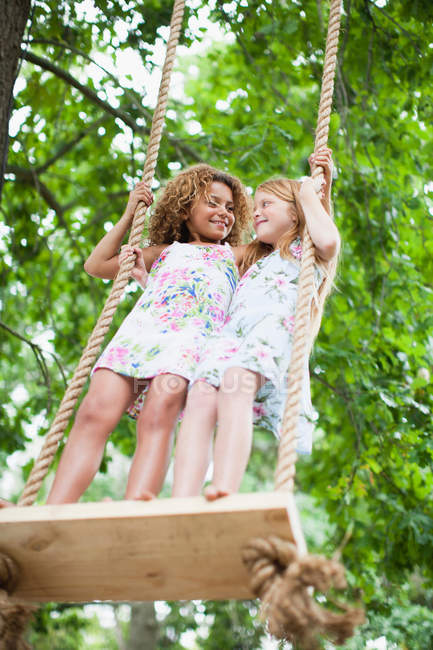 Smiling girls standing on tree swing — Stock Photo
