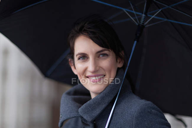 Femme souriante sous parapluie, se concentrer sur le premier plan — Photo de stock