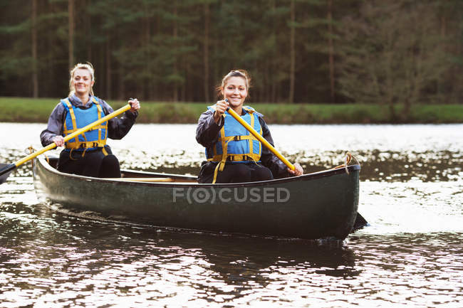 Mulheres remando canoa em lago imóvel — Fotografia de Stock