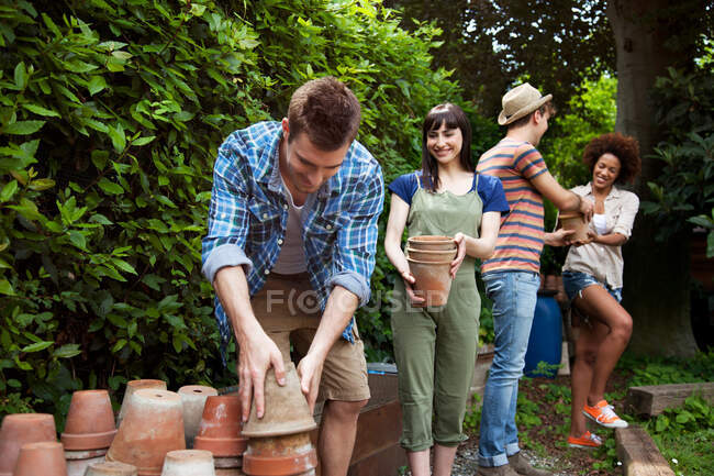 Quatre amis empilant des pots de plantes en terre cuite — Photo de stock