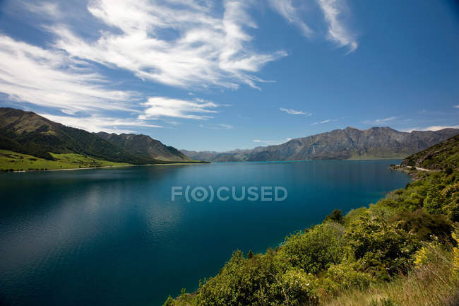 Lac calme avec des montagnes sous un ciel nuageux bleu — Photo de stock