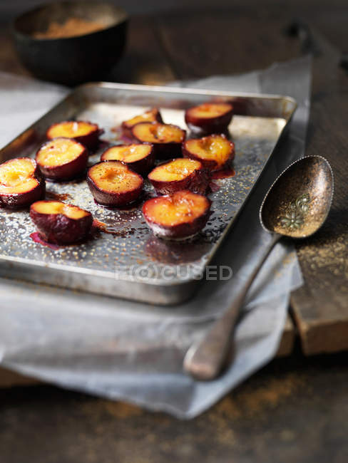 Tray of baked plum halves with spoon — Stock Photo