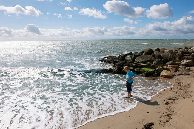 Хлопчик стоїть в серфінгу на пляжі — стокове фото