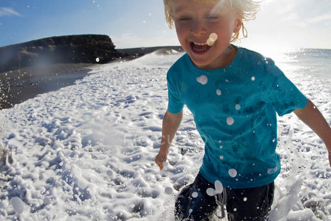 Menino brincando em ondas na praia — Fotografia de Stock