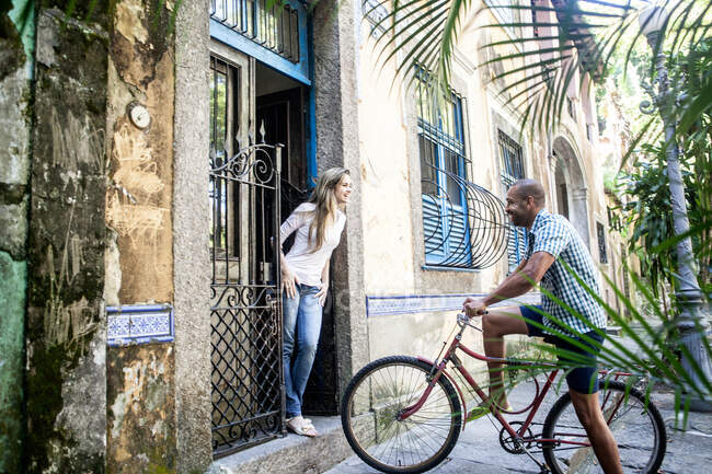Мужчина на велосипеде разговаривает с женщиной в дверях, Рио-де-Жанейро, Бразилия — стоковое фото
