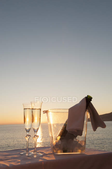 Champagne flutes and bucket with bottle against sunset — Stock Photo