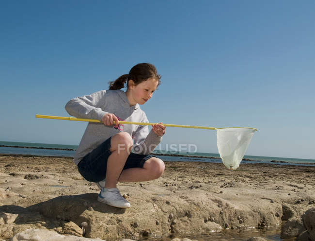 Girl playing with fishing net on beach — Stock Photo