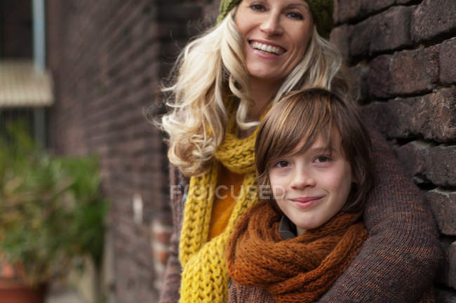 Madre e hijo sonriendo contra la pared de ladrillo, retrato - foto de stock