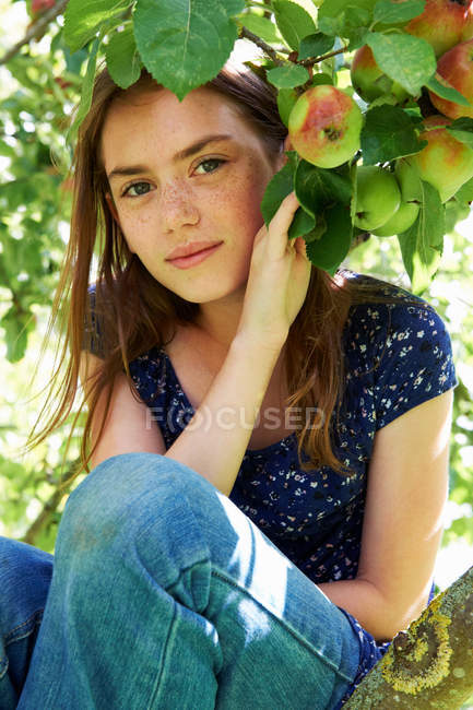 Chica sonriente sentada en un árbol frutal - foto de stock
