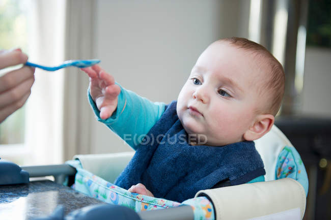 Baby reaching for spoon at table — Stock Photo