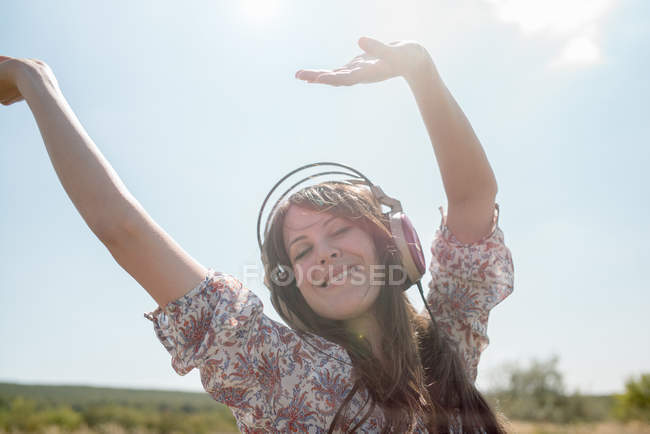 Портрет середньої дорослої жінки, яка танцює в полі в навушниках з піднятими руками — стокове фото