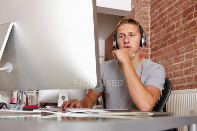 Hombre joven que trabaja en la computadora con auriculares - foto de stock