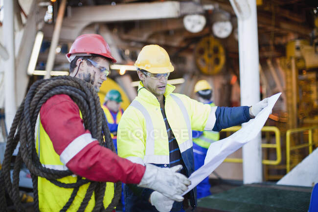 Trabajadores examinando planos en plataforma petrolera - foto de stock
