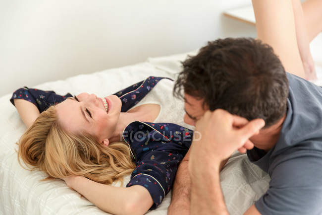 Couple reclining on bed and smiling to each other at home — Stock Photo