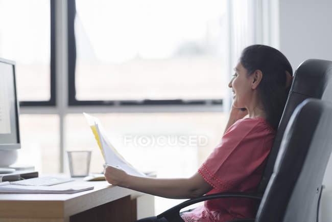 Woman holding papers and sitting at workplace table and talking on mobile phone — Stock Photo