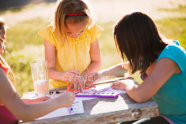 3 young girls sitting at table painting — Stock Photo