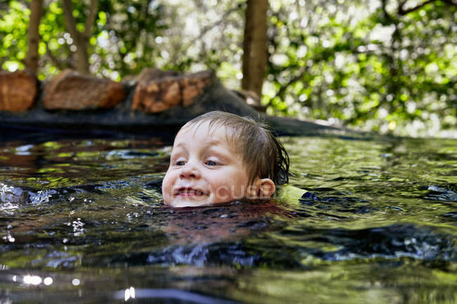 Close up of boy swimming in river in forest — Stock Photo