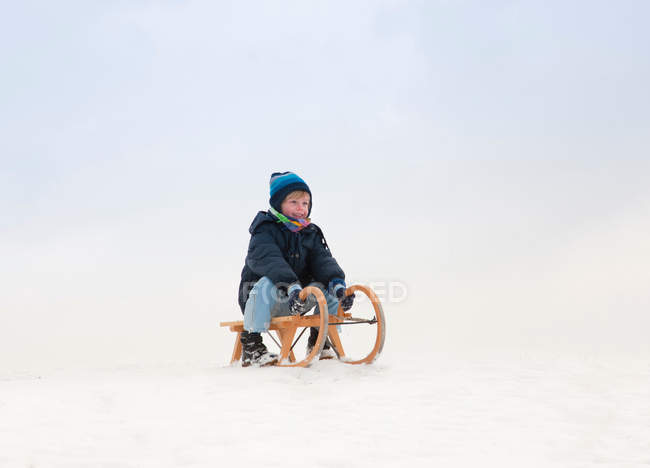 Boy sitting on sled in snow — Stock Photo