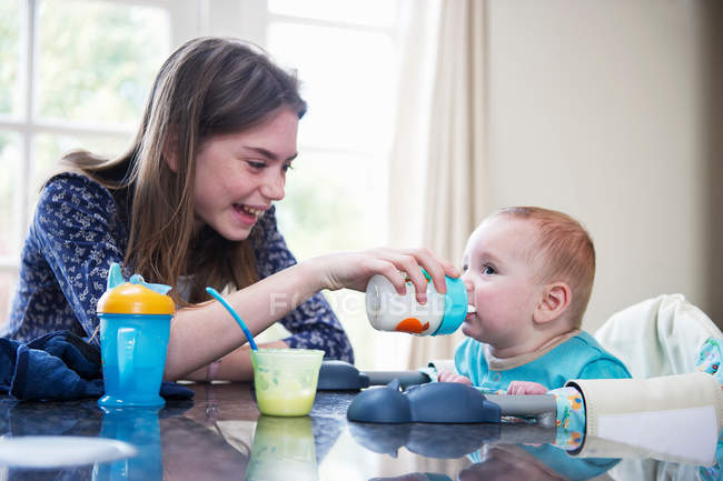 Girl feeding baby brother at table — Stock Photo