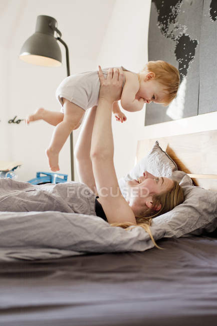 Mid adult woman holding up baby daughter in bed — Stock Photo