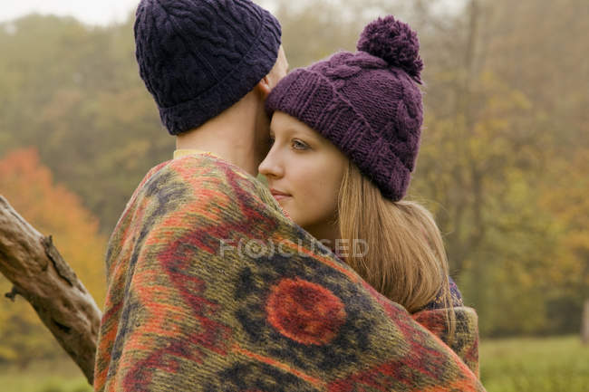 Close up de jovem casal envolto em cobertor no parque nebuloso — Fotografia de Stock