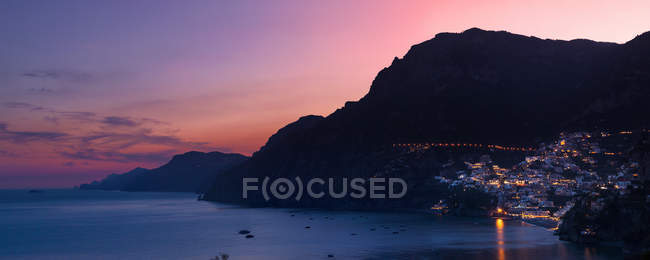 Edificios laterales acantilados en bahía iluminados por la noche, Positano, Costa Amalfitana, Italia - foto de stock