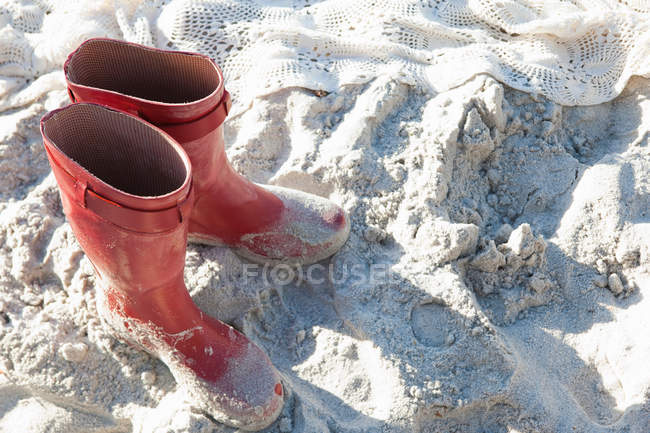 Bottes de pluie et couverture sur sable éclairé par le soleil — Photo de stock