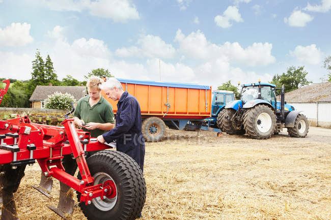 Farmers adjusting machinery in field — Stock Photo
