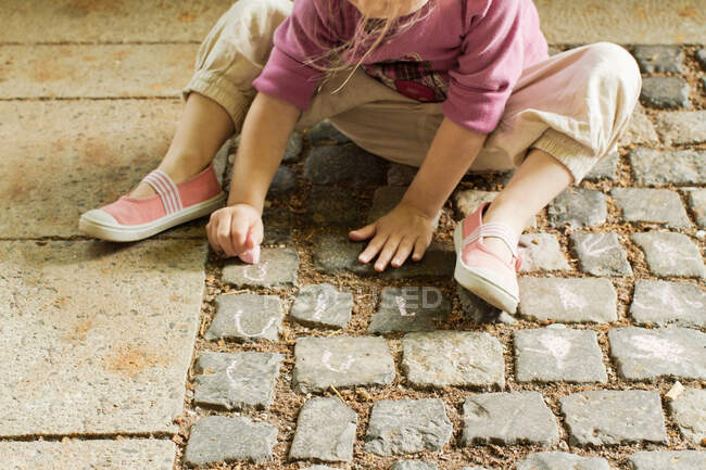 Girl drawing with chalk on cobblestone — Stock Photo