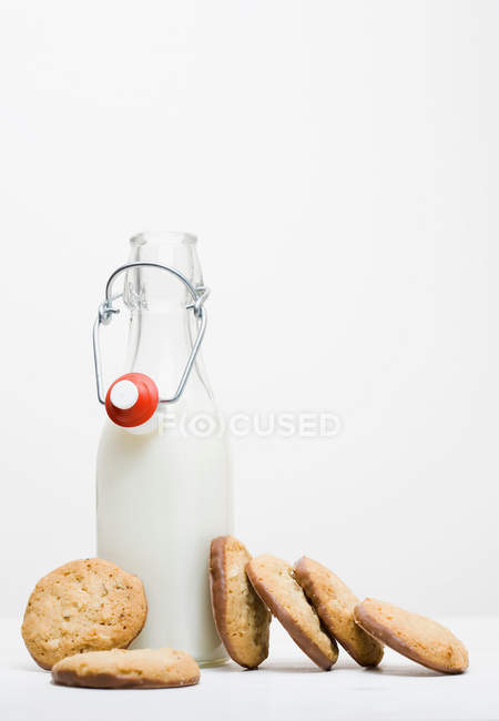 Печенье со стеклянной бутылкой молока на белом фоне — стоковое фото