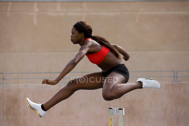 Läuferin springt auf Bahn über Hürden — Stockfoto