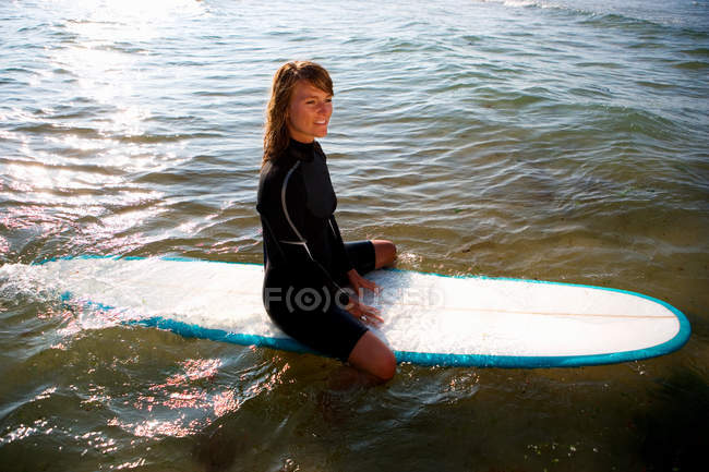 Femme assise sur une planche de surf souriant — Photo de stock