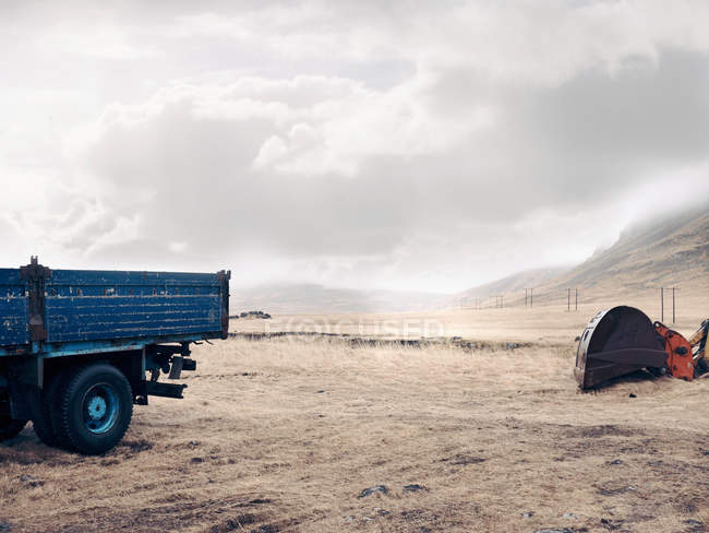 Camión azul y excavadora en campo seco con cielo nublado - foto de stock