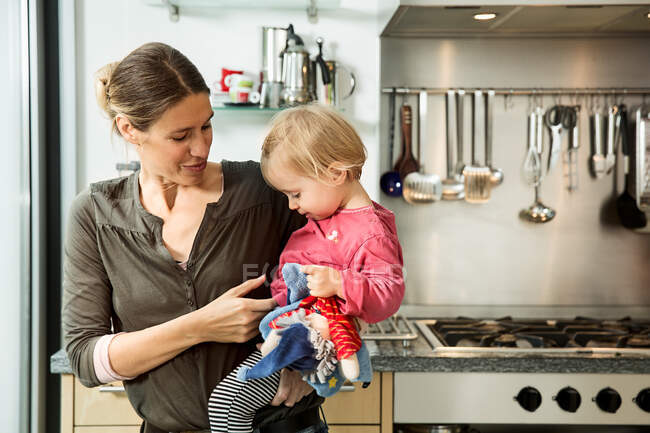 Mother carrying baby girl in kitchen — Stock Photo